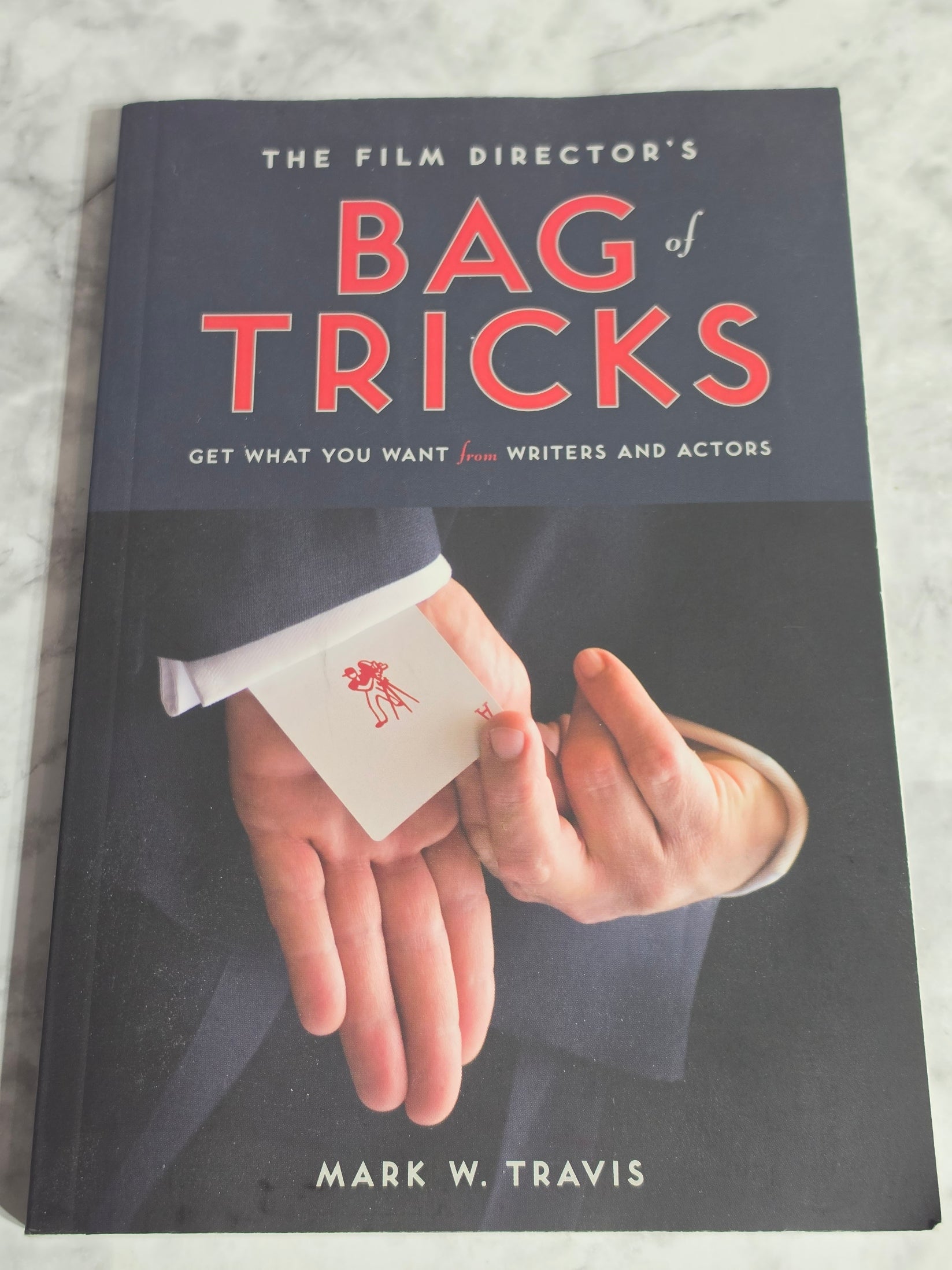 Book cover of 'The Film Director's Bag of Tricks' by Mark W. Travis on a marble surface.