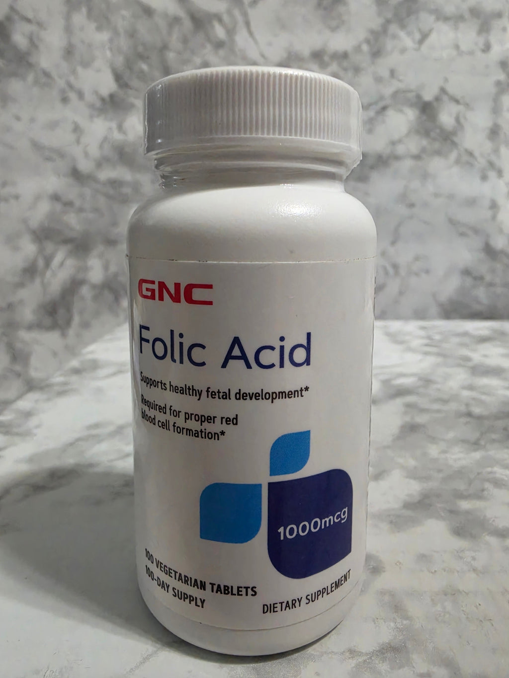 GNC Folic Acid supplement bottle on a marble surface