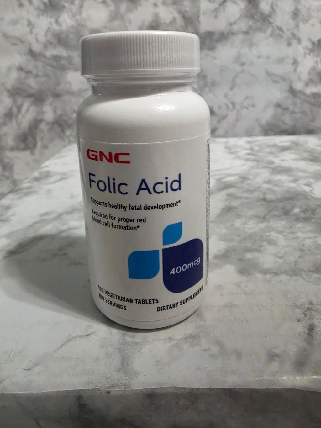 GNC Folic Acid supplement bottle on a marble surface