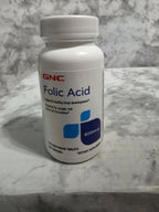 GNC Folic Acid supplement bottle on a marble surface