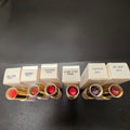 Six Mary Kay High Profile lipstick shades beside their labeled cartons, from Sunny Coral to Black Raspberry