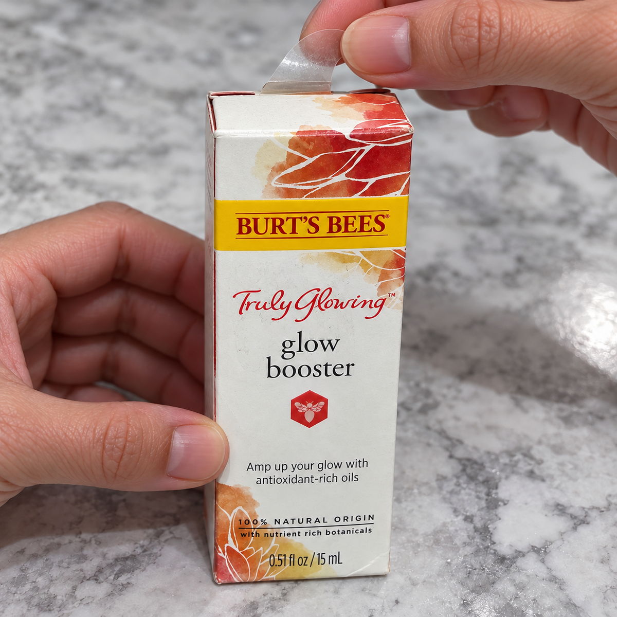 Adult hands opening Burt's Bees Truly Glowing Glow Booster carton, AI-assisted illustration