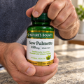 AI-generated illustration: adult hands gripping the cap and bottle of Nature’s Bounty Saw Palmetto 450 mg, 100 Capsules.