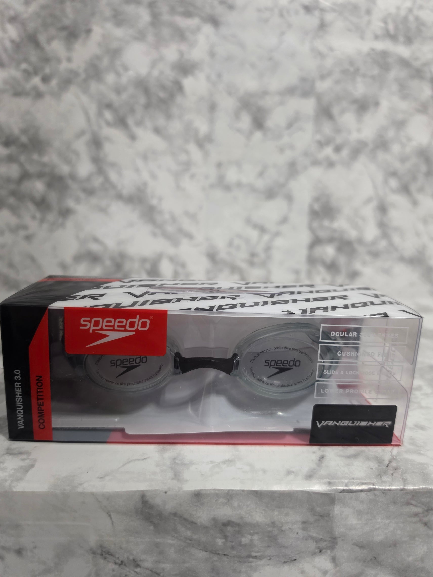 Packaged swimming goggles with visible brand logos on a marble surface