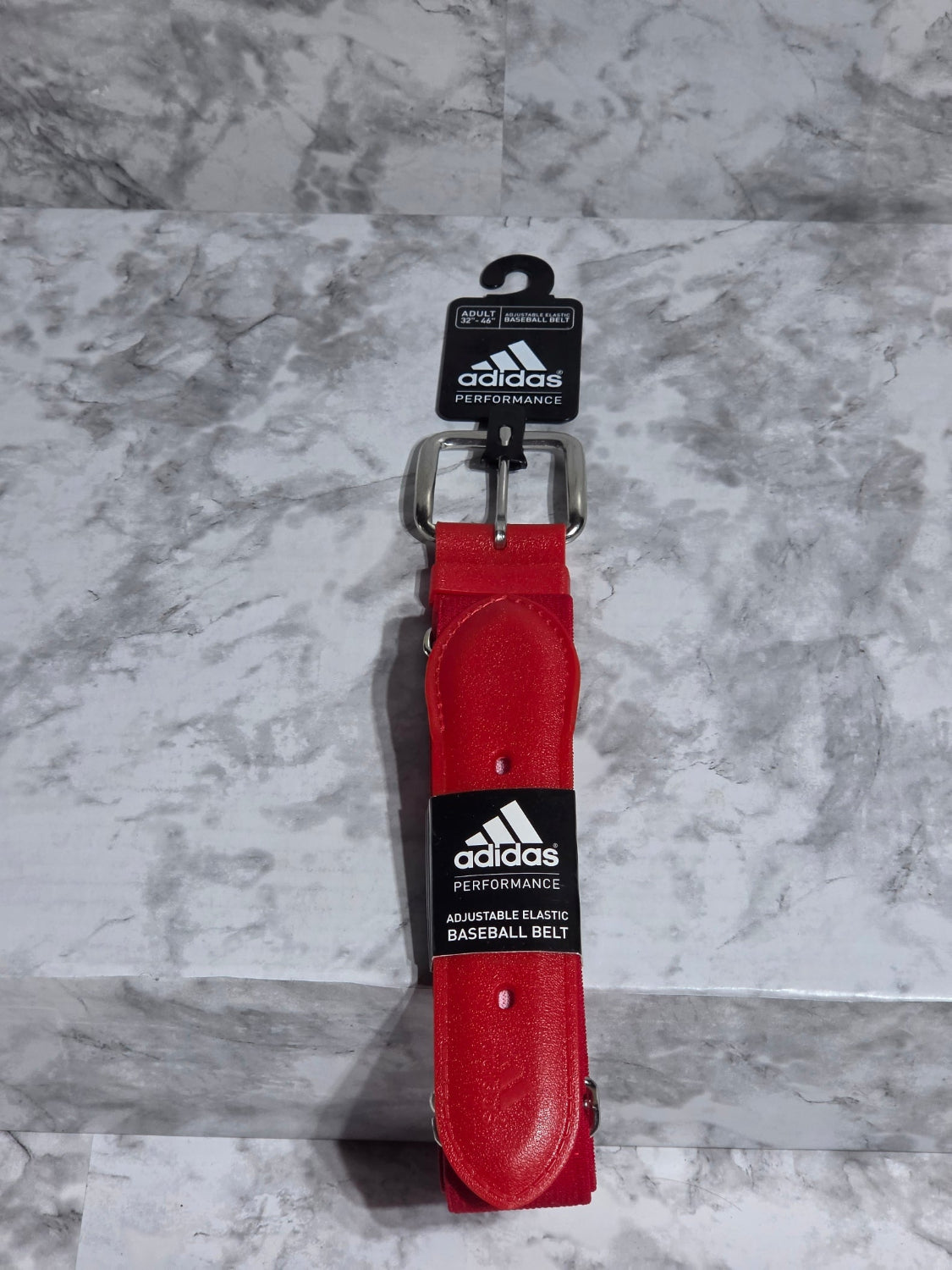 Red baseball belt with Adidas logo on a gray marble surface