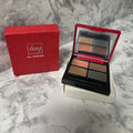 Open Avon fmg Glimmer Siren eyeshadow quad with four shades, mirror and applicator beside its red box on a marble-pattern background.