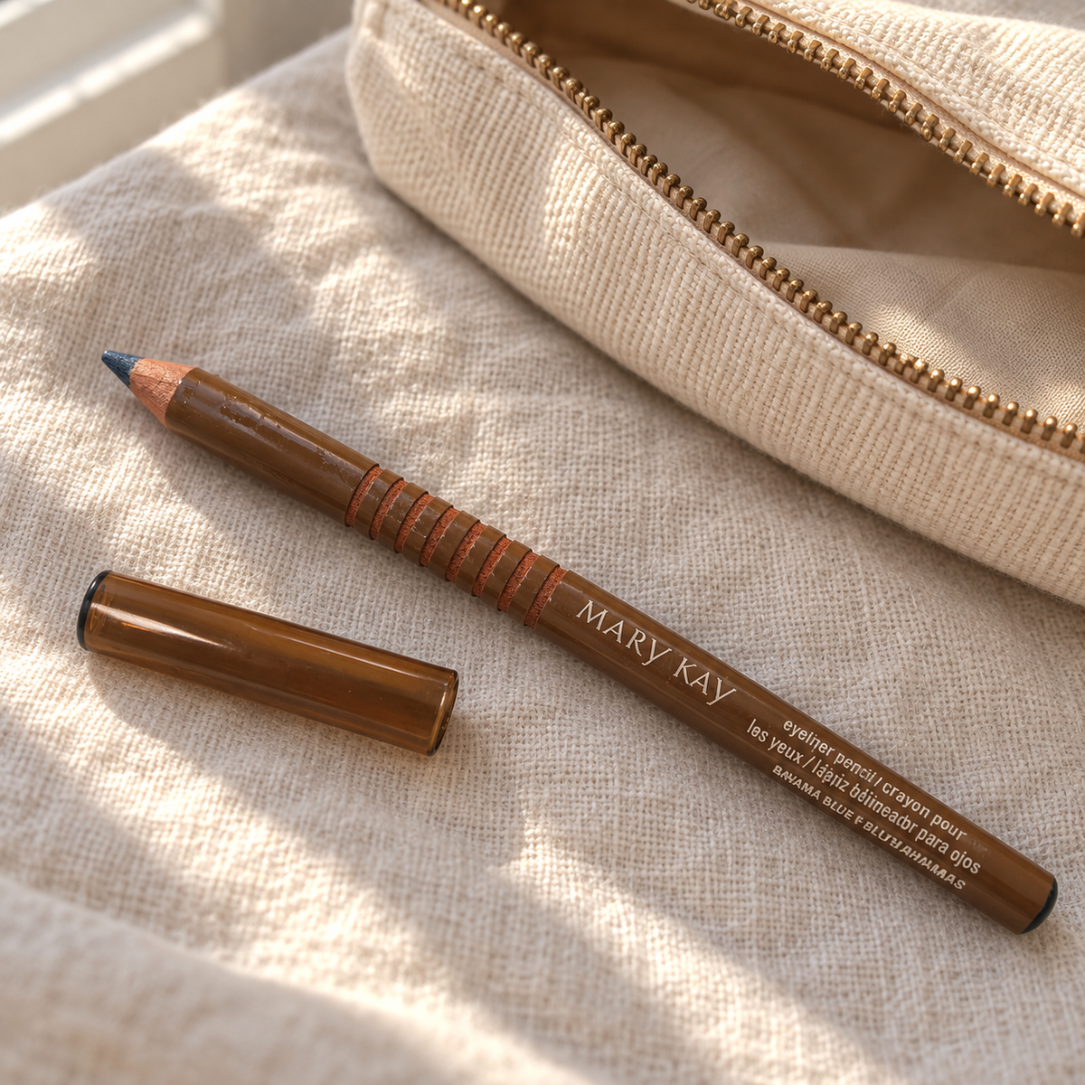 Mary Kay Bahama Blue eyeliner pencil with its cap beside a canvas travel pouch