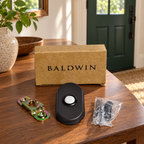 AI lifestyle illustration: Baldwin Oil Rubbed Bronze Arch doorbell kit, bracket, bagged fasteners and box on a walnut entry console