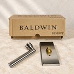 AI-generated product illustration: Baldwin Reserve Tube lever and separate rectangular rose with original box on a stone surface; not the actual stock photograph.