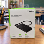 Belkin AVC005 USB-C multimedia adapter retail box in a classroom desk setting, AI-assisted lifestyle illustration.
