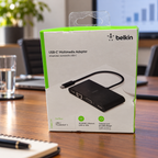 Belkin AVC005 USB-C multimedia adapter retail box in a conference room setting, AI-assisted lifestyle illustration.