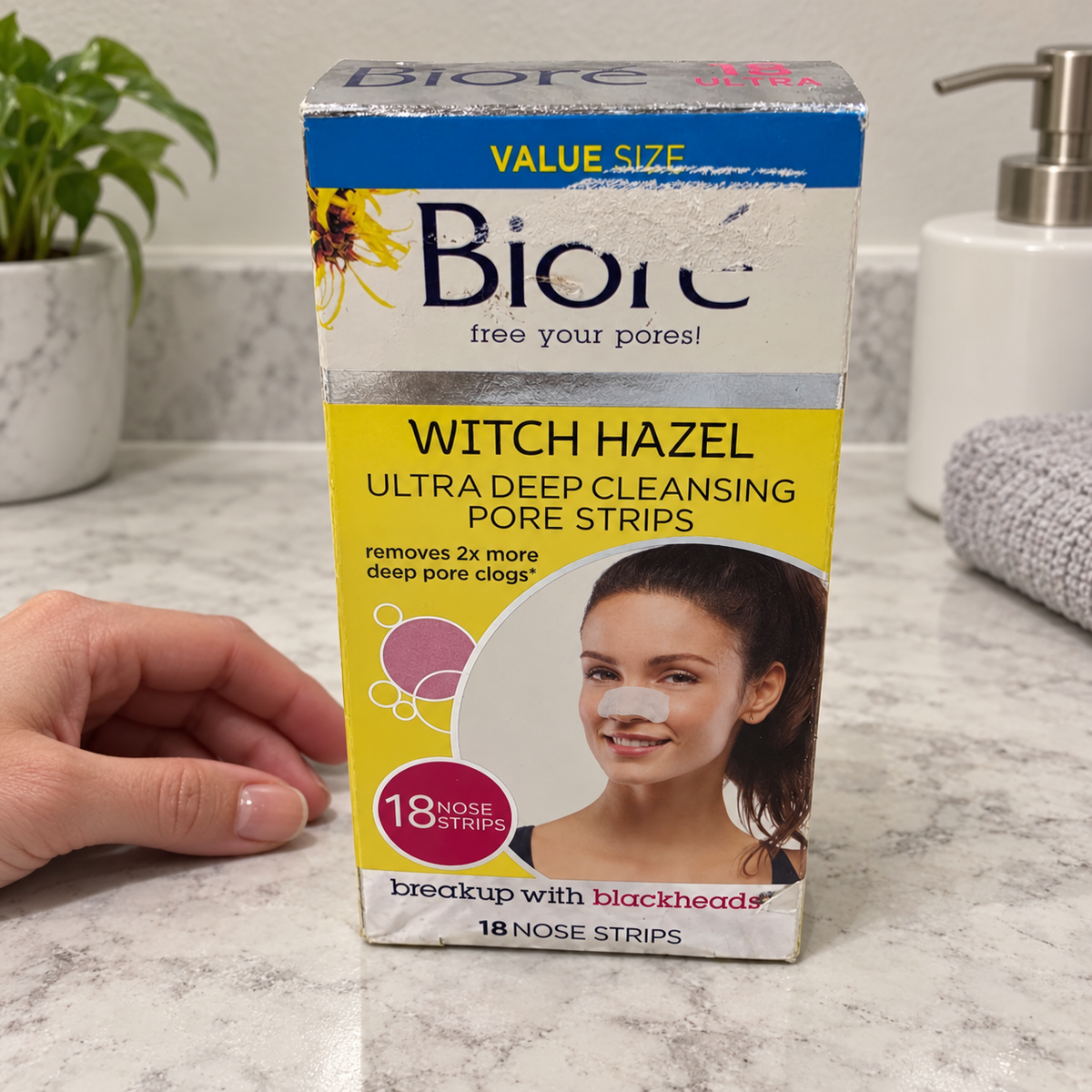AI-generated bathroom counter scene of the worn Bioré Witch Hazel 18-strip box beside an adult hand.
