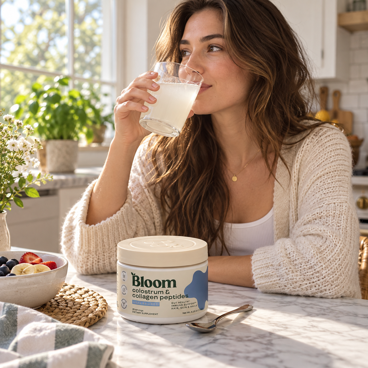 Woman drinking a mixed beverage with Bloom Colostrum and Collagen Peptides nearby