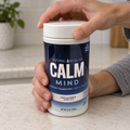 Hands opening a CALM Mind Unflavored drink-mix tub.