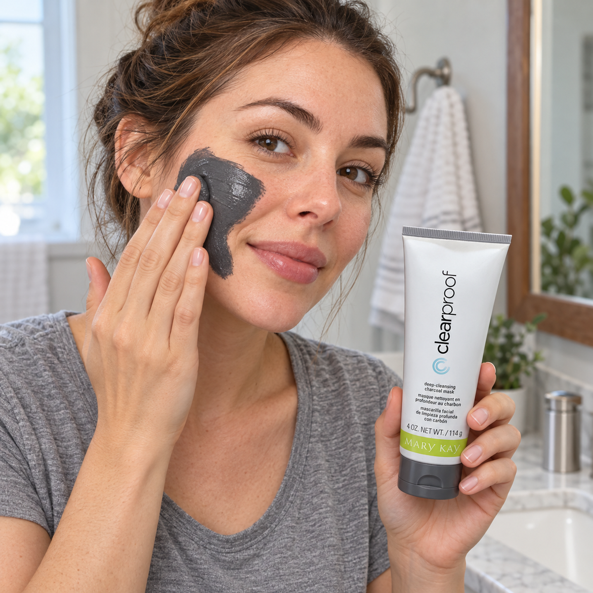 Applying a charcoal-gray mask to the cheek while holding the Mary Kay Clear Proof tube