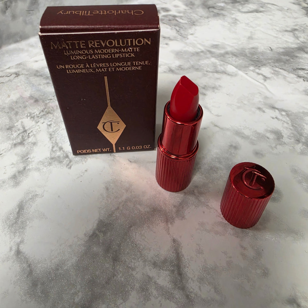 Charlotte Tilbury Hollywood Vixen mini lipstick with open red tube, cap and original box on a marble-pattern background