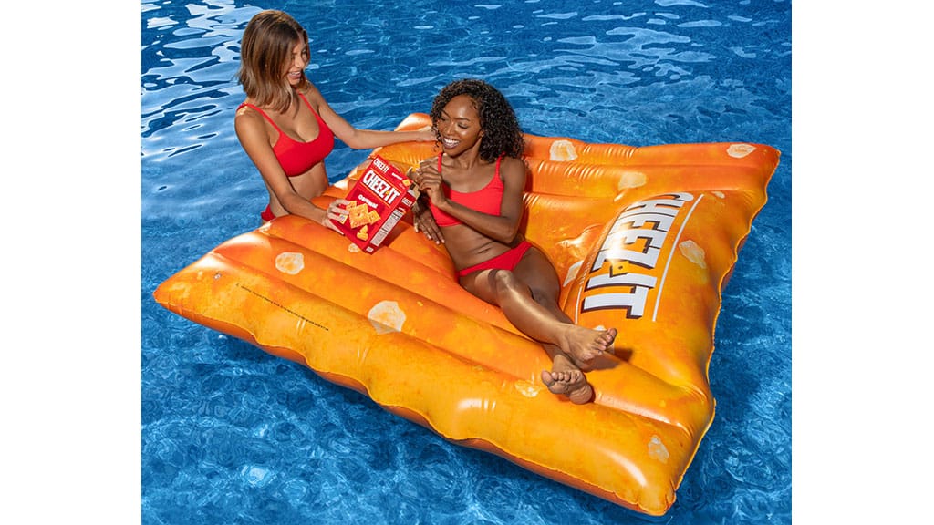Adult relaxing on a Cheez-It Original pool float with another adult alongside in a swimming pool.