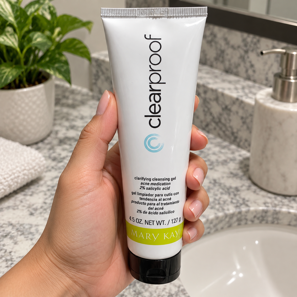 Holding a capped Mary Kay Clear Proof 127 g cleansing gel tube by the bathroom sink