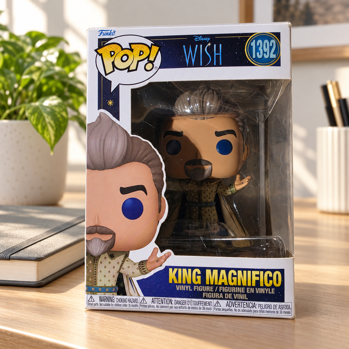 Funko Pop! King Magnifico #1392 in its original Disney Wish box on a clean modern desk beside a closed neutral notebook