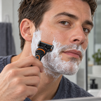 An adult shaving his cheek with an old-design Gillette Fusion5 cartridge on a compatible handle.