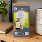 GE Link A19 daylight LED bulb carton in household shelf setting; AI-generated lifestyle illustration