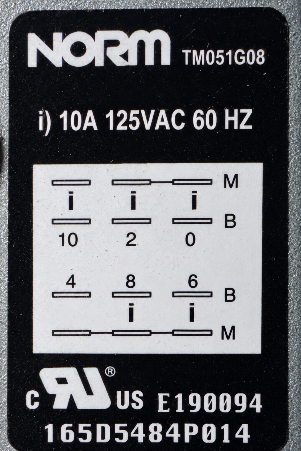Close detail of the stocked GE dishwasher timer rating label showing NORM TM051G08, 10A 125VAC 60Hz and terminal diagram