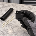 Black capacitor housing held by a gloved hand with sleeve and ties nearby