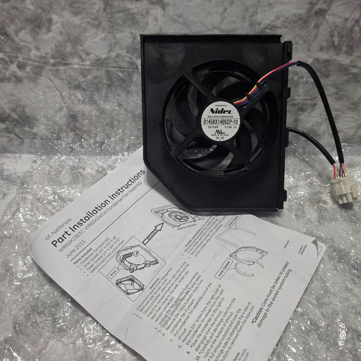 Actual inventory photo: GE WR60X23363 fan assembly, original Nidec motor label, wiring connector and included instruction sheet