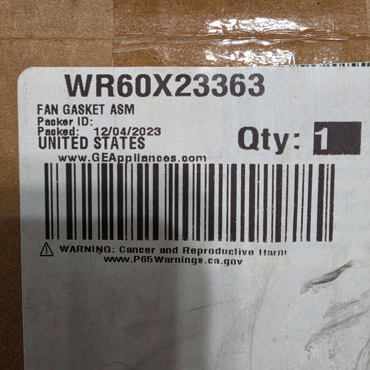 Actual inventory photo: original GE box label reading WR60X23363 FAN GASKET ASM, quantity 1, with the manufacturer warning