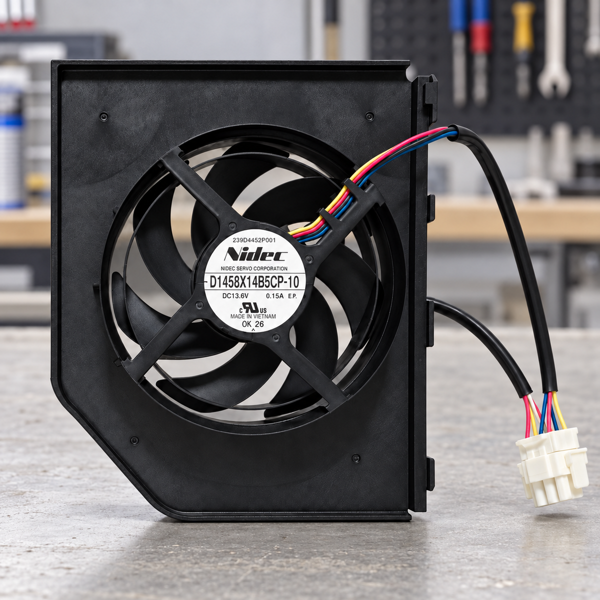 GE WR60X23363 condenser fan assembly with wiring connector on an appliance workshop bench; illustrative setting, background tools not included