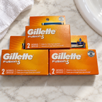 Three Gillette Fusion5 two-cartridge boxes, six refills total, on a white marble bathroom vanity; lifestyle setting.