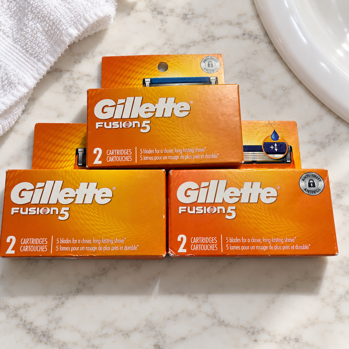 Three Gillette Fusion5 two-cartridge boxes, six refills total, on a white marble bathroom vanity; lifestyle setting.