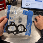 Packaged GM gasket held beside a laptop during part-number planning.