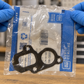 GM water-pump gasket in its original clear bag held by gloved hands for inspection.