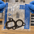 GM water-pump gasket in its original clear bag held by gloved hands for inspection.