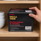 A hand placing the closed GNC Mega Men Performance & Vitality carton on a wooden cupboard shelf.