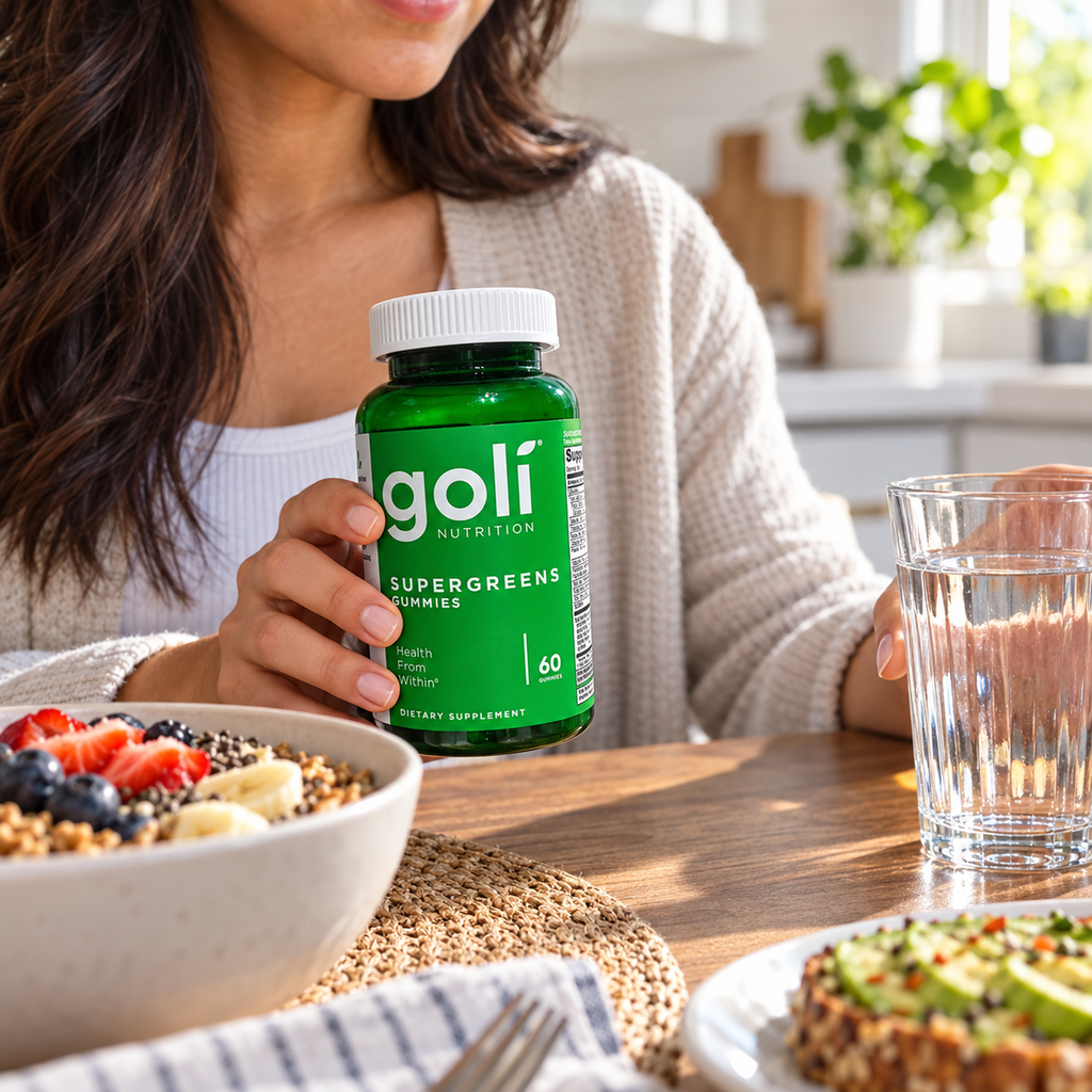 Holding Goli Supergreens gummies beside breakfast