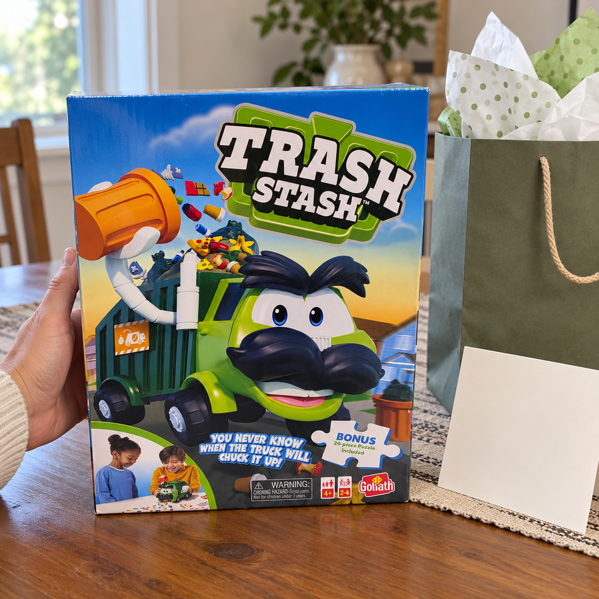 Goliath Trash Stash bonus-puzzle game box beside gift-wrapping props.