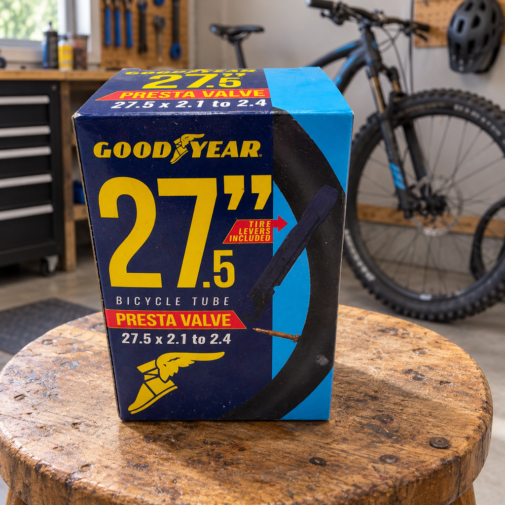 Goodyear 27.5 x 2.1–2.4 Presta valve bicycle tube package on a wooden stool in a bike garage; AI-staged lifestyle scene.