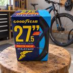 Goodyear 27.5 x 2.1–2.4 Presta valve bicycle tube package on a wooden stool in a bike garage; AI-staged lifestyle scene.