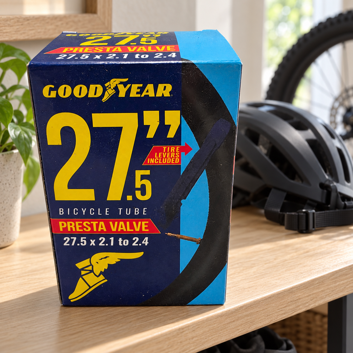 Goodyear 27.5 x 2.1–2.4 Presta valve bicycle tube package on a cycling gear shelf near a helmet; AI-staged lifestyle scene.