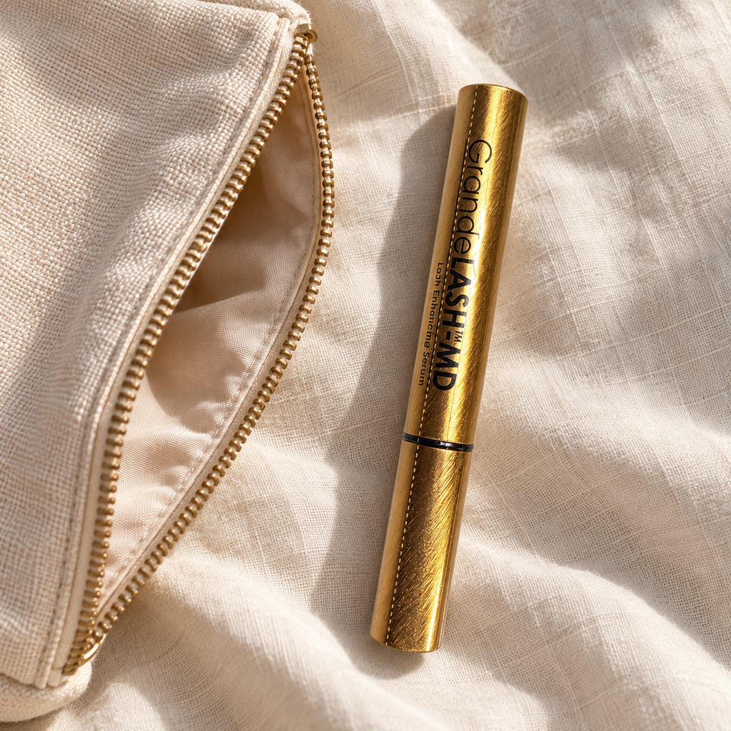 GrandeLASH-MD 2 mL gold serum tube beside an ivory makeup pouch on linen