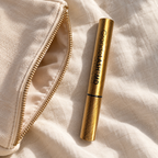 GrandeLASH-MD 2 mL gold serum tube beside an ivory makeup pouch on linen