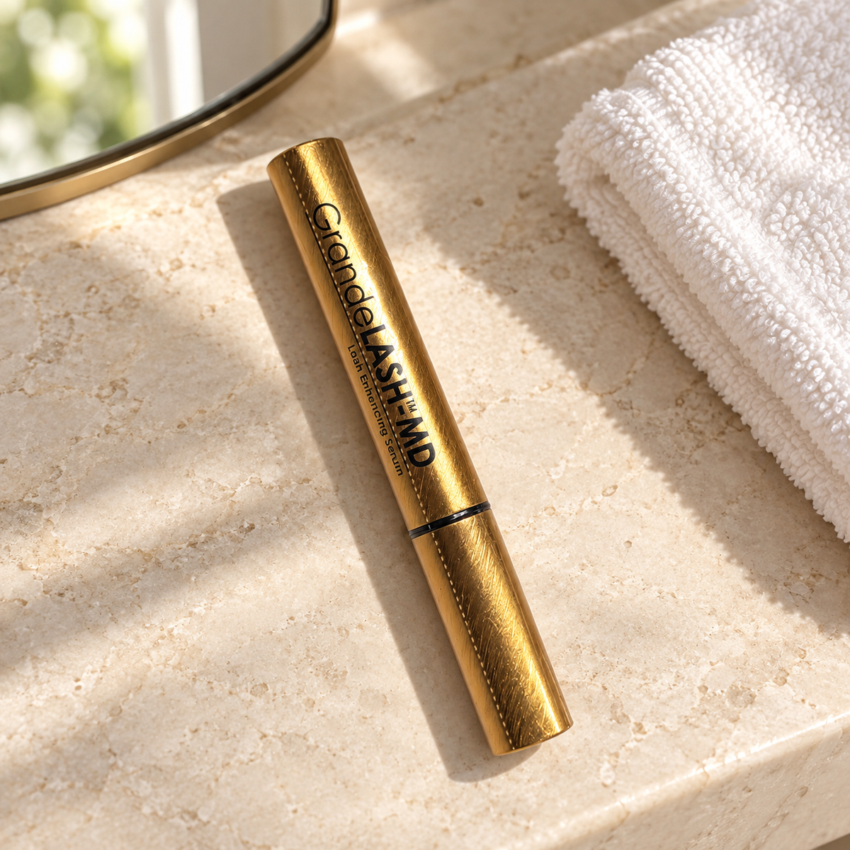 GrandeLASH-MD gold serum tube on a stone vanity beside a white washcloth