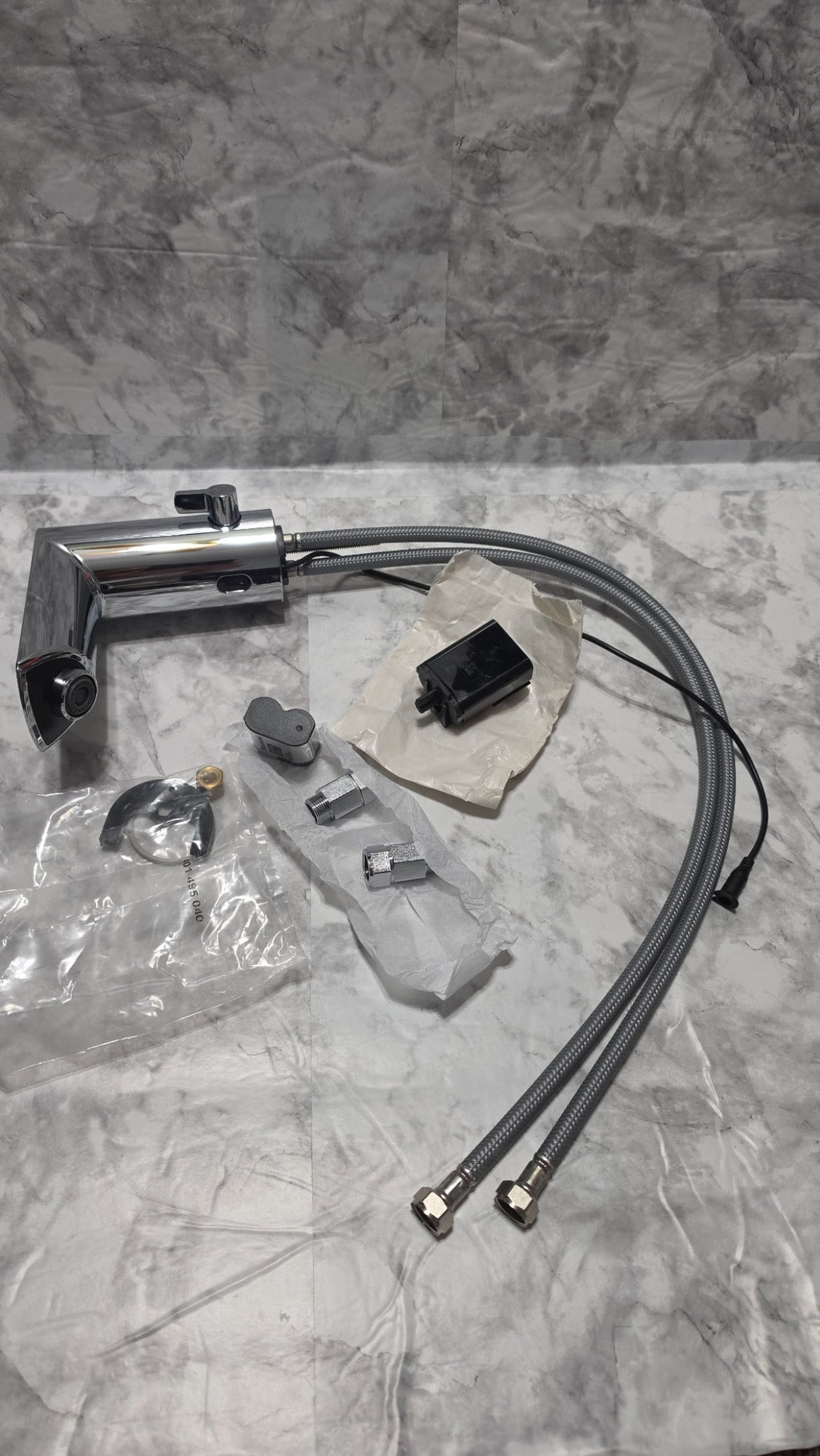 Actual inventory photo: unboxed GROHE faucet with battery and holder, two hoses, mounting hardware and two inlet fittings; no AC adapter