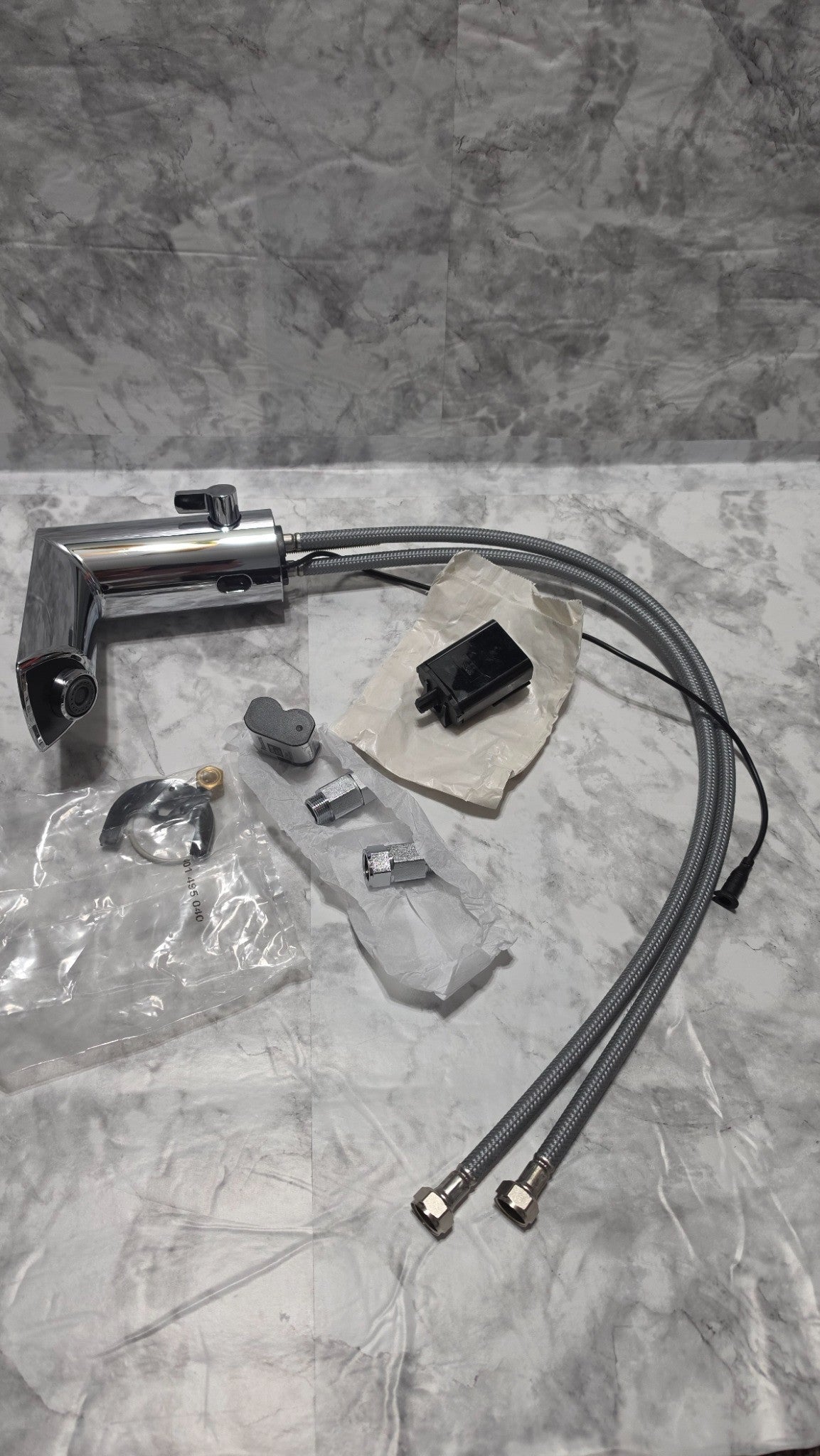 Actual inventory photo: unboxed GROHE faucet with battery and holder, two hoses, mounting hardware and two inlet fittings; no AC adapter