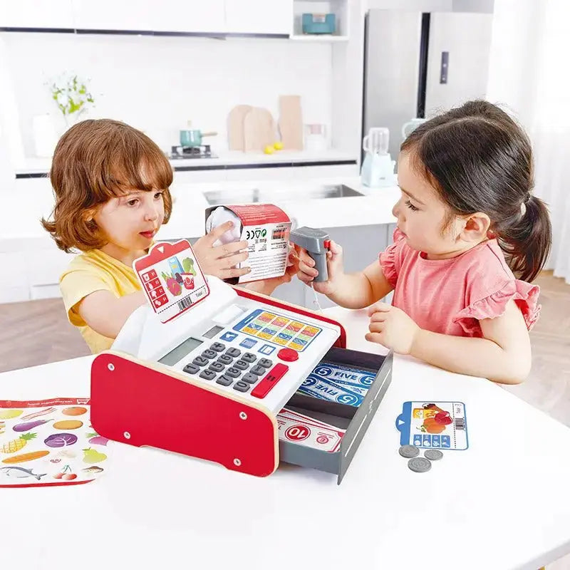 Two children using a Hape Beep n Buy E3184 cash register for pretend checkout at a table.