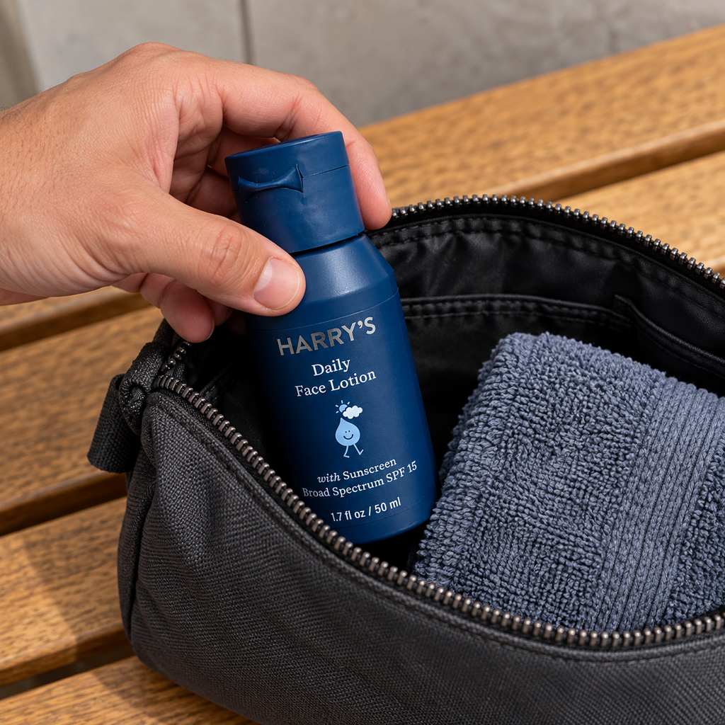 A hand placing the closed Harry's Daily Face Lotion bottle in a toiletry bag.