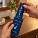 Hands lifting a closed Harry's Daily Face Lotion bottle from its blue carton.