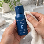 Hands wiping the outside of the closed Harry's Daily Face Lotion bottle with a cloth.